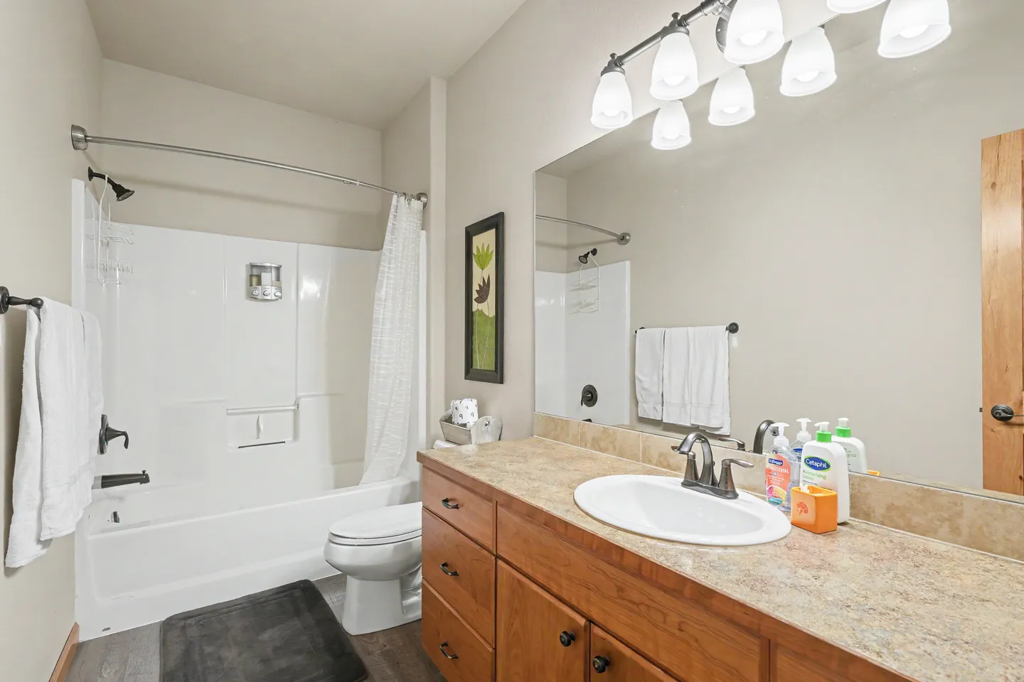 Bathroom with a wood vanity, large mirror with vanity lighting, toilet, and combination bathtub and shower.