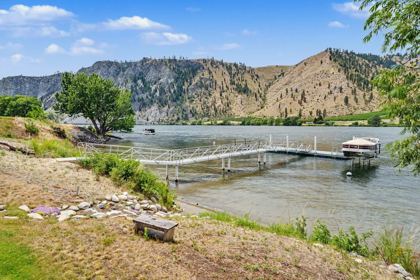 A long private boat dock extending into a wide river with a boat lift, backed by arid hills and blue sky.