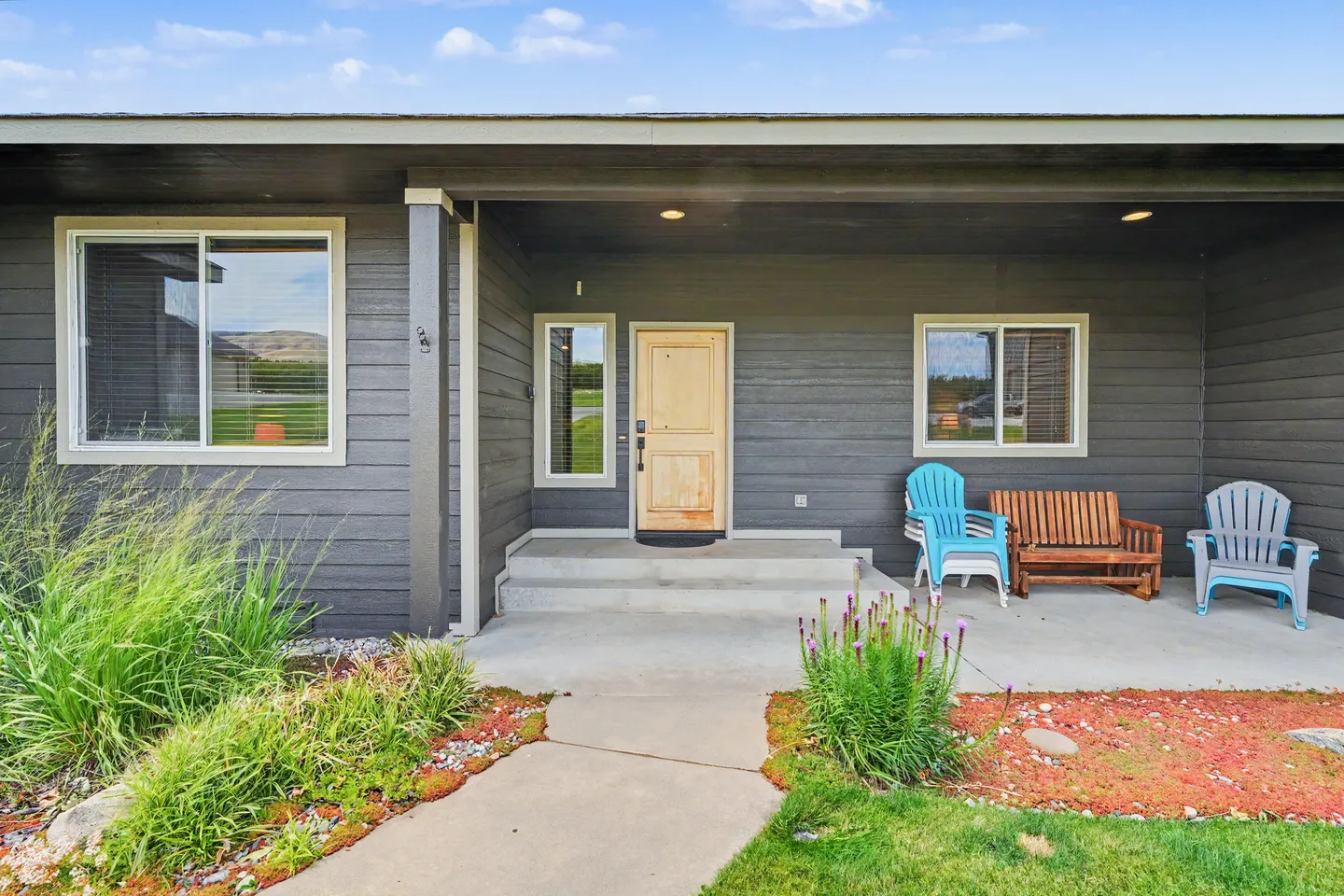 Front porch of a dark grey home with a natural wood door and outdoor seating.