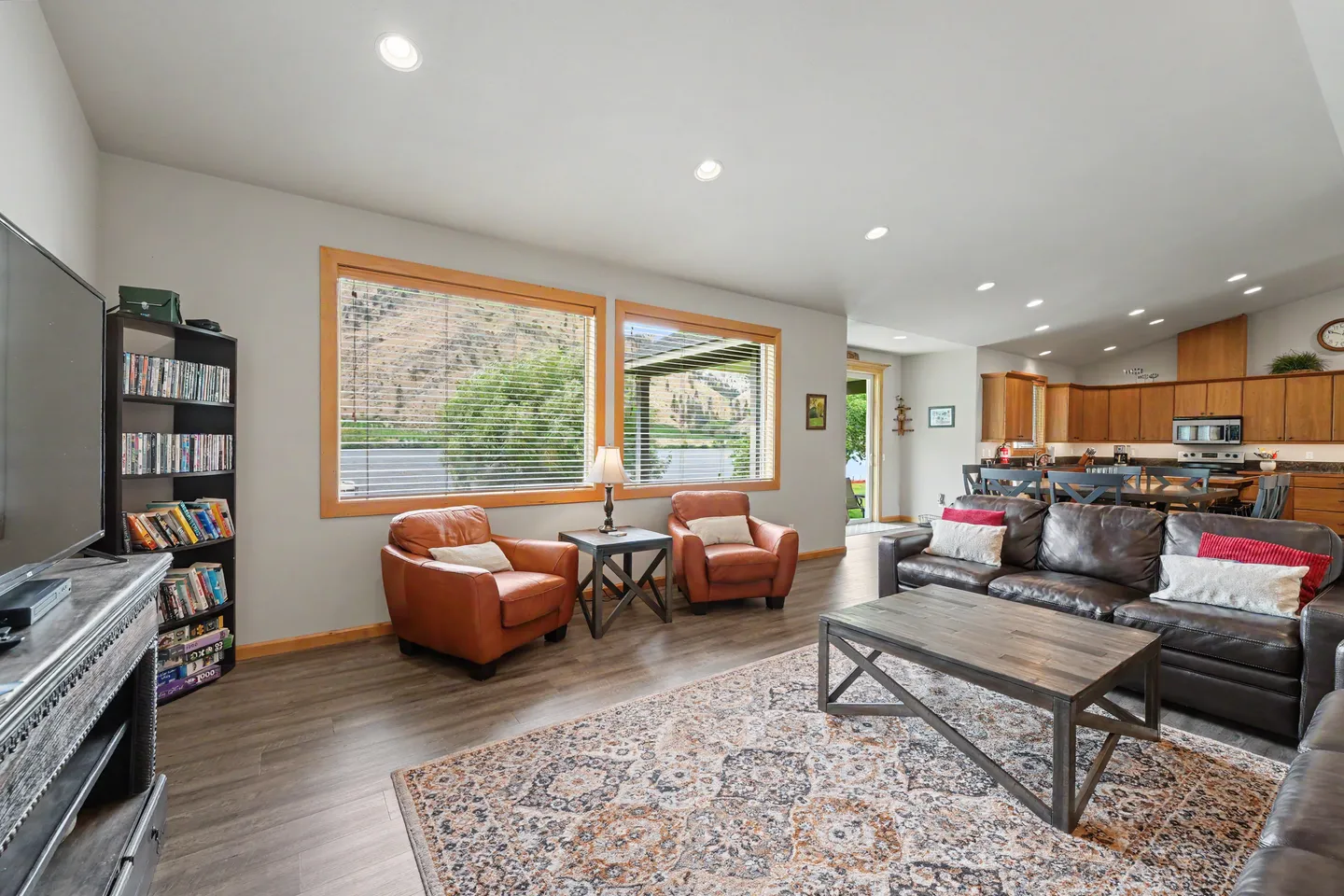 Open-concept living room with leather seating, patterned area rug, coffee table, and an open view into the kitchen and dining area.