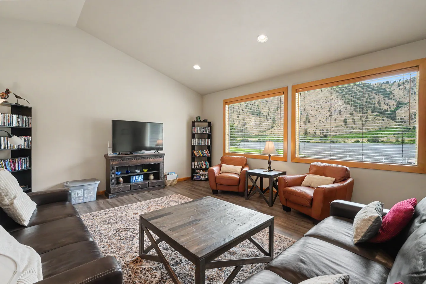 Living room with leather sofas, armchairs, a television, and large windows overlooking a scenic hill.