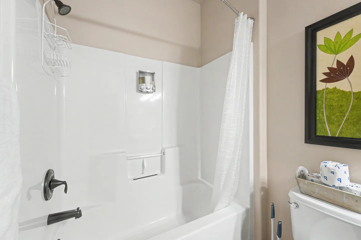 Bathroom showing a white bathtub and shower combo with dark fixtures, white shower curtain, and adjacent toilet.