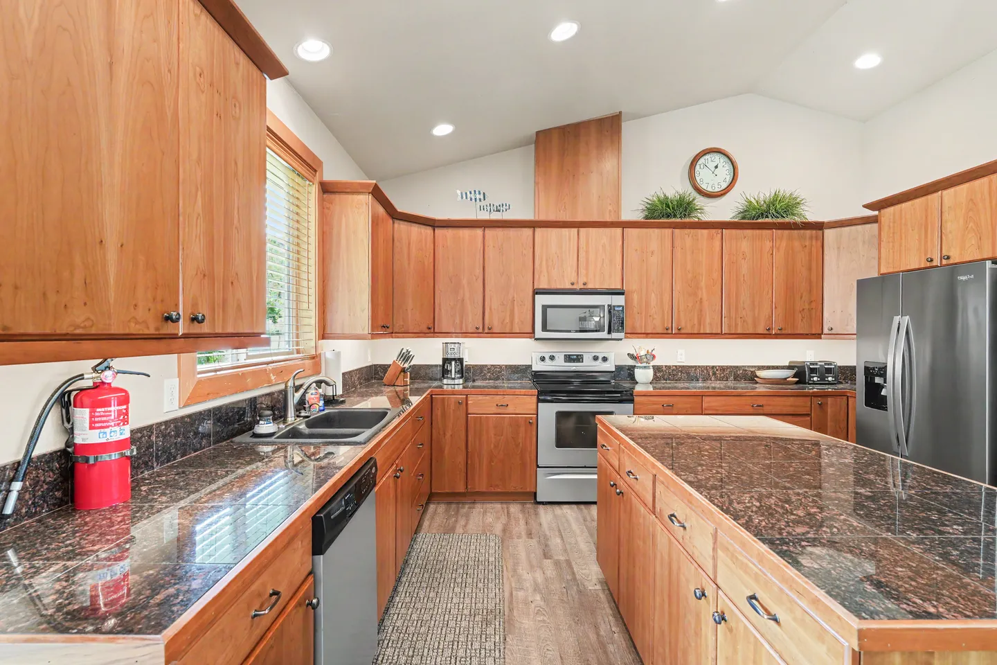 Spacious kitchen featuring warm wood cabinetry, polished granite countertops, a central island, and stainless steel appliances.
