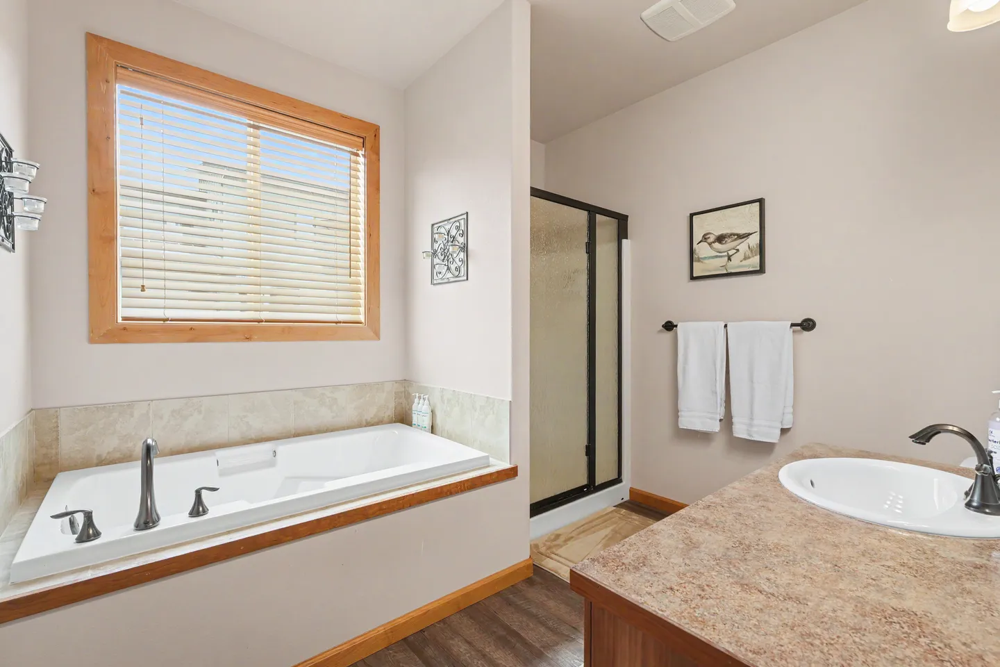 Bathroom with a drop-in soaking tub beneath a wood-trimmed window, a glass shower stall, and a vanity sink.