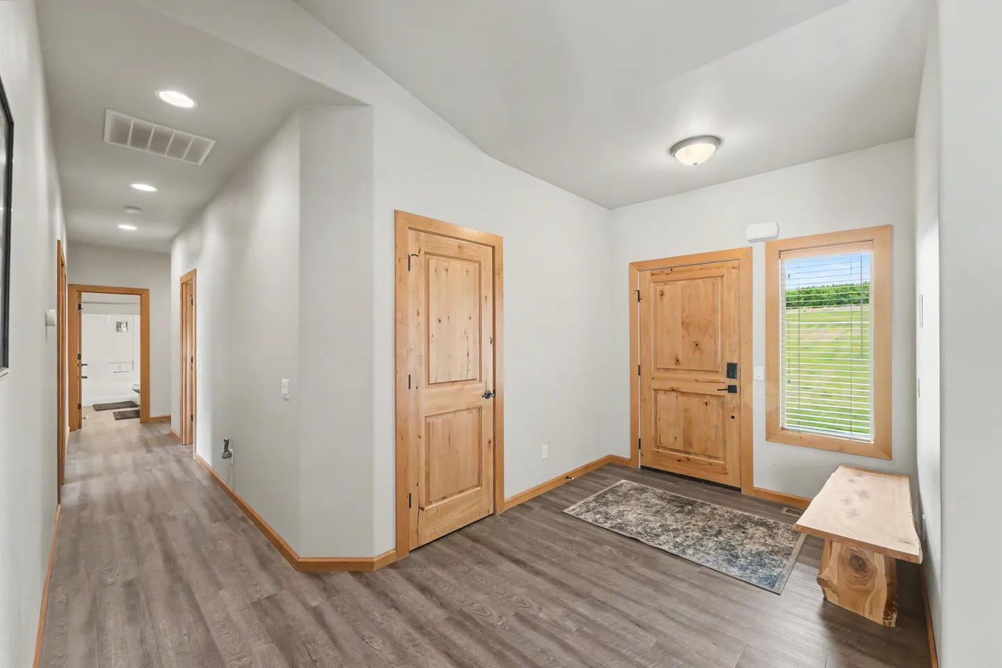 Front entryway with wood door, window, rustic bench, and a long hallway with wood-look flooring.