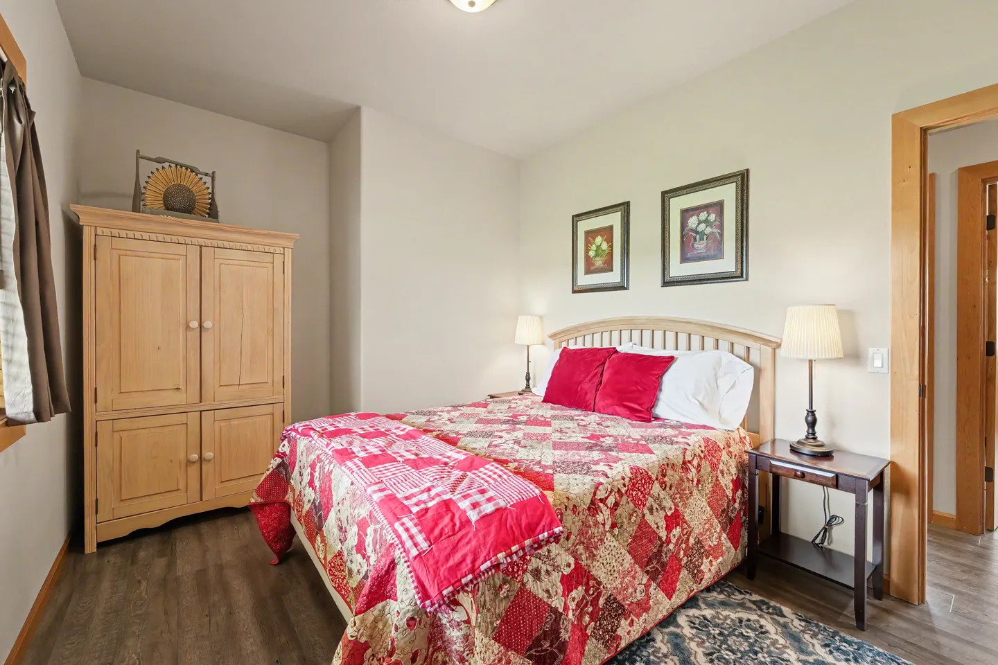 Bedroom with a wooden headboard, red patchwork quilt, nightstand with a lamp, and a large wooden armoire.