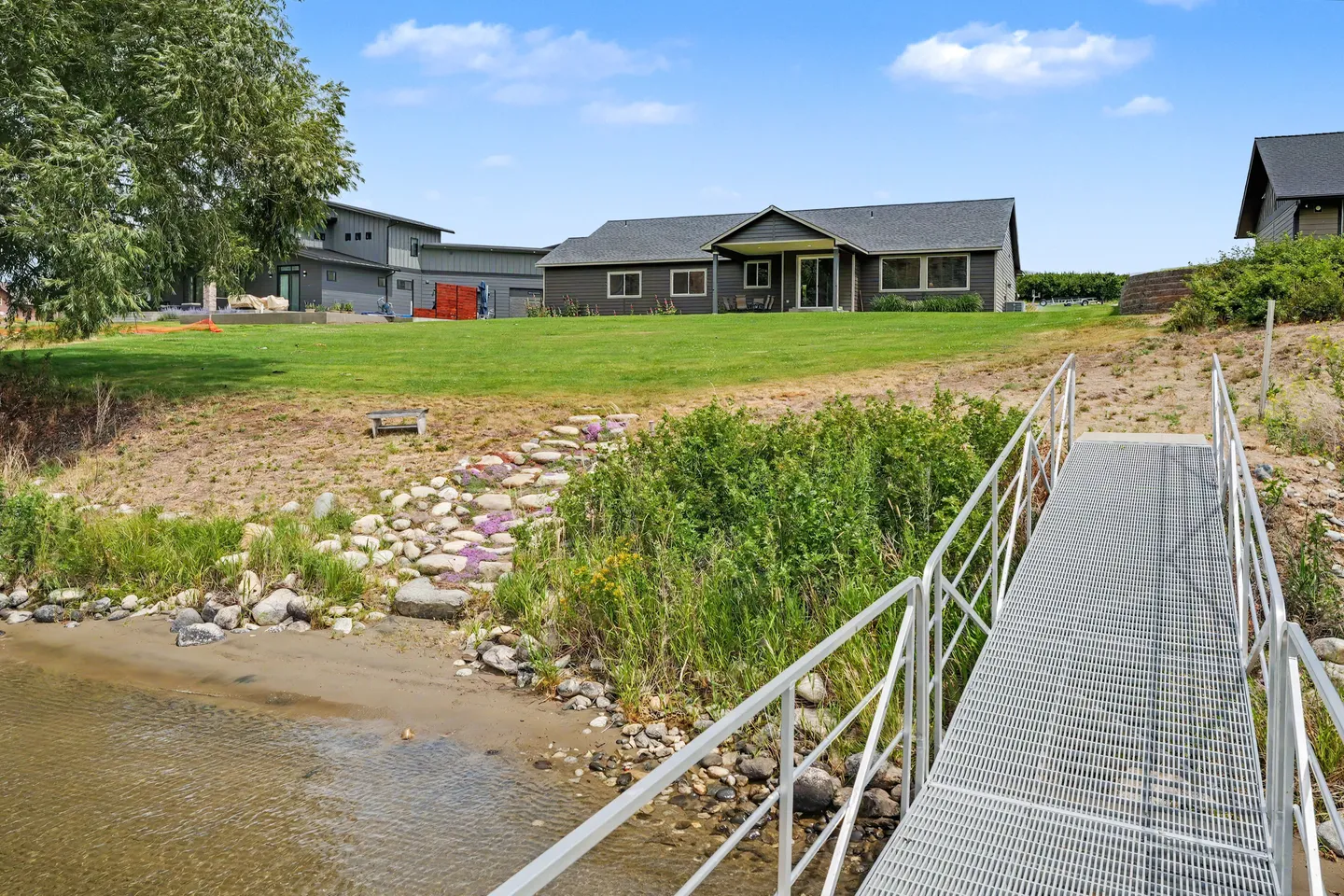 View from a metal dock walkway looking up a grassy yard toward a single-story house with dark siding.