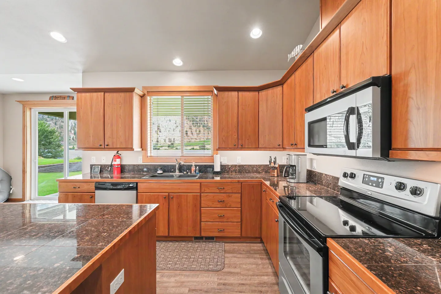 Kitchen with wooden cabinetry, dark countertops, an electric range, and a window above the sink.