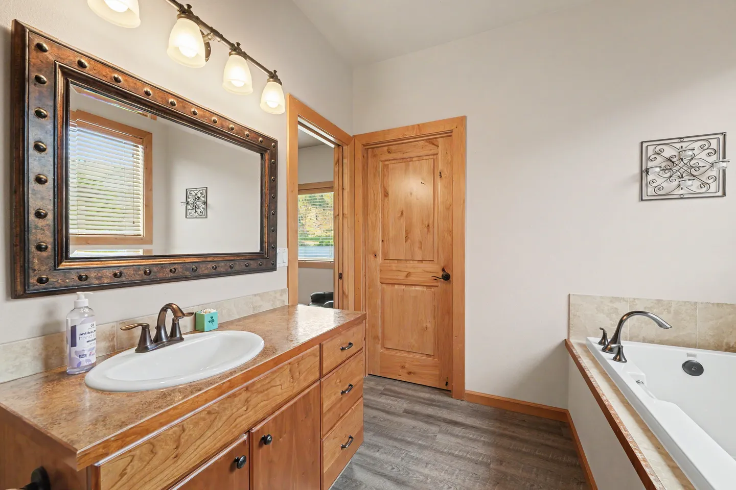 Bathroom with a wood vanity, studded metal-look framed mirror, and a soaking tub.