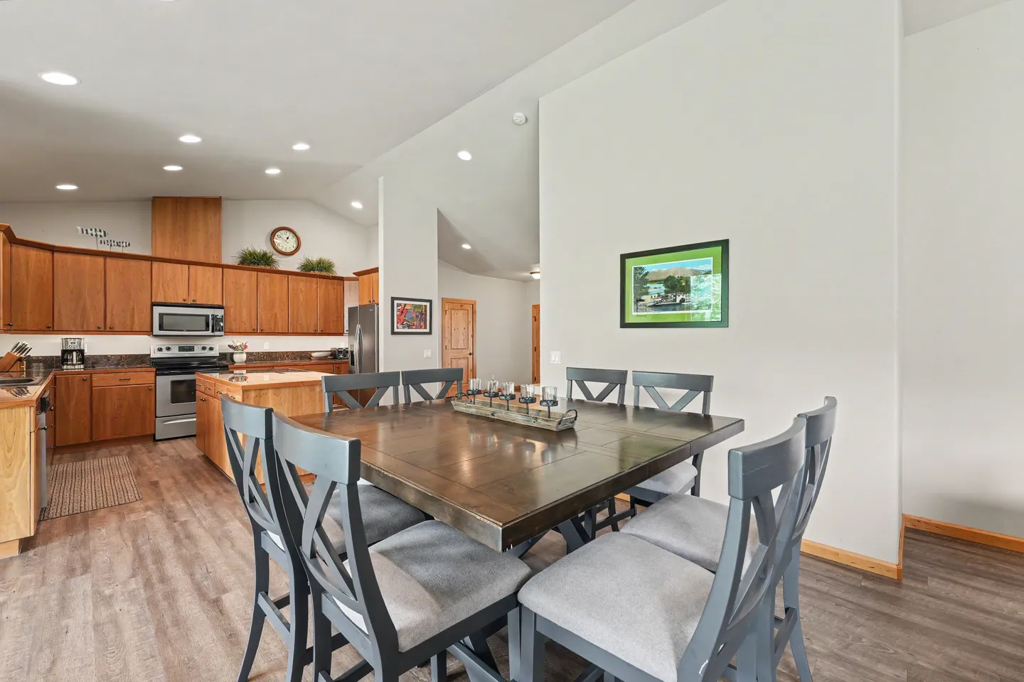 Dining area with a large wooden table and grey chairs adjacent to an open-concept kitchen.