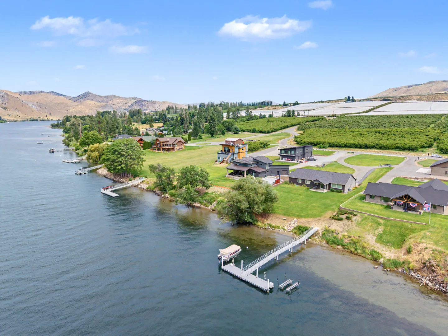 Aerial view of a lakefront neighborhood featuring private boat docks, green lawns, and surrounding hills.
