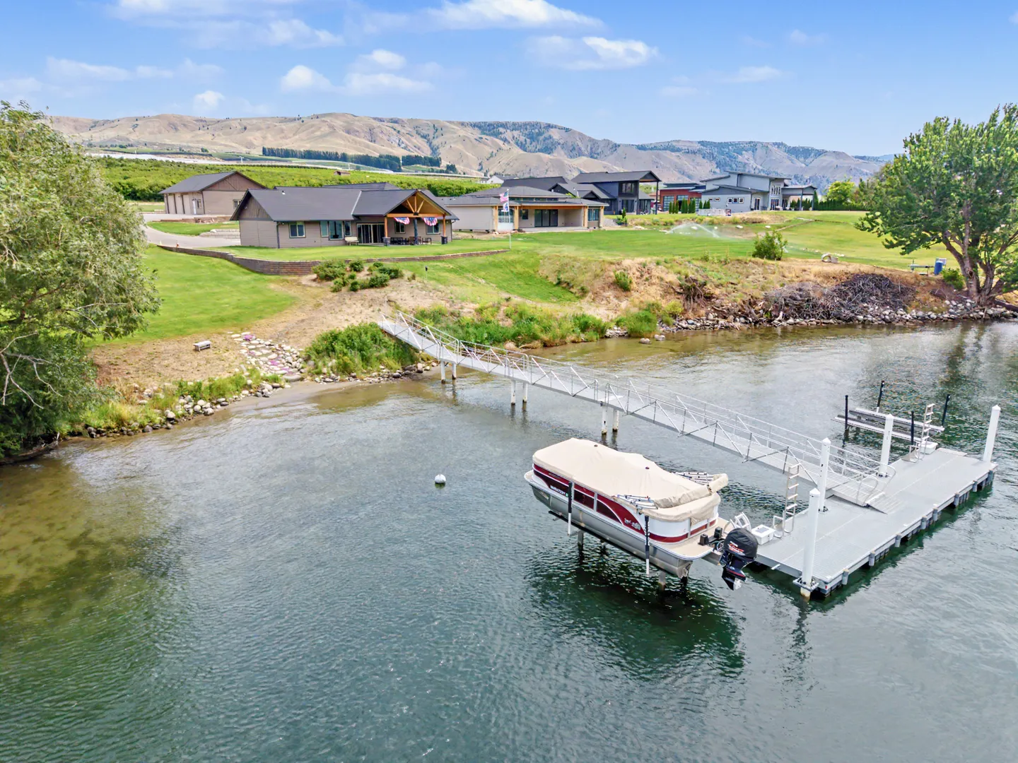 Aerial view of a waterfront home with a grassy lawn, a long private gangway, and a floating boat dock with a pontoon boat lift.
