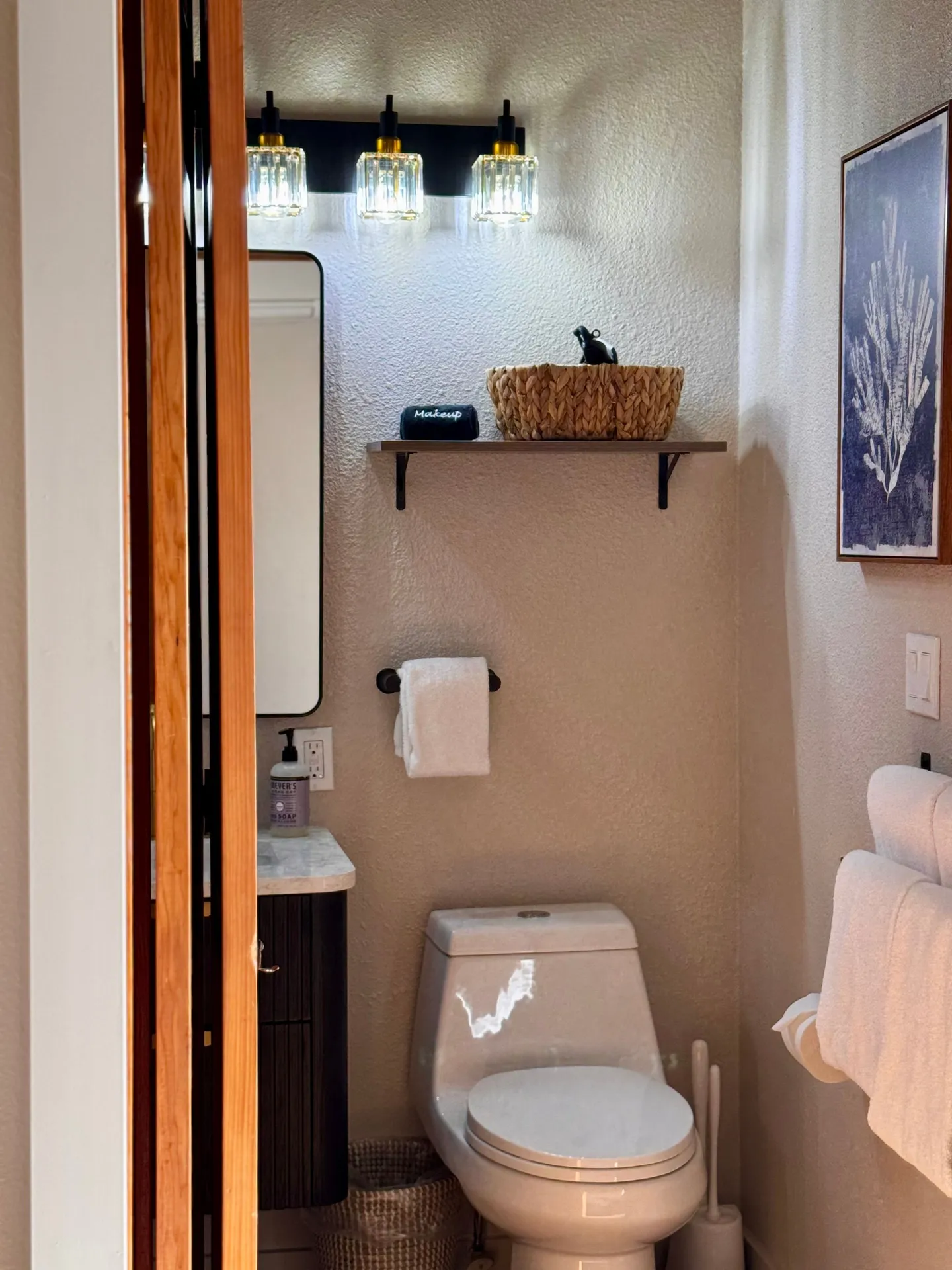 Powder room with a white toilet, small vanity, floating wall shelf, and modern vanity light fixture.