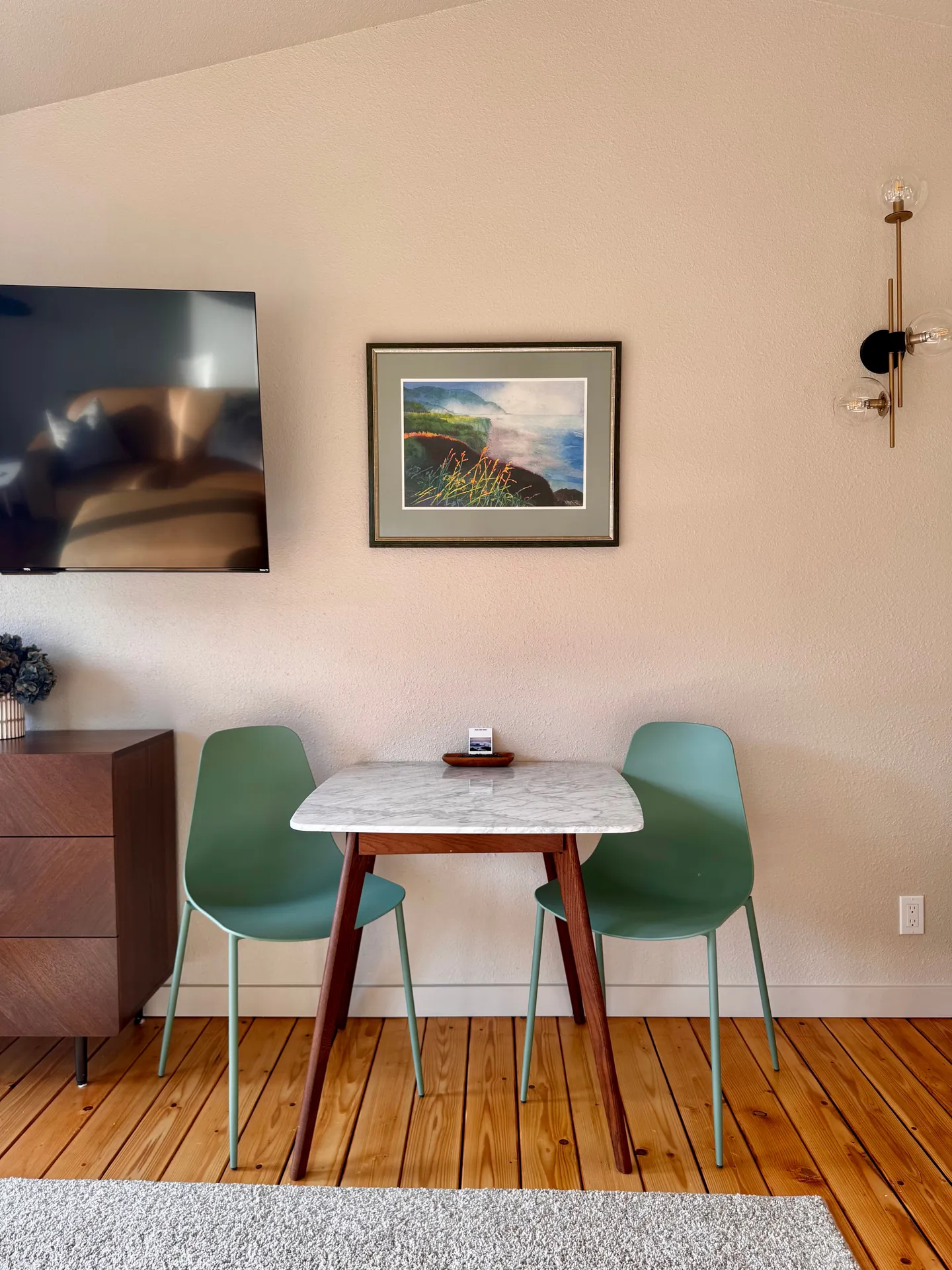 A small dining or seating area with two sage green chairs and a marble-top table set against a neutral wall.