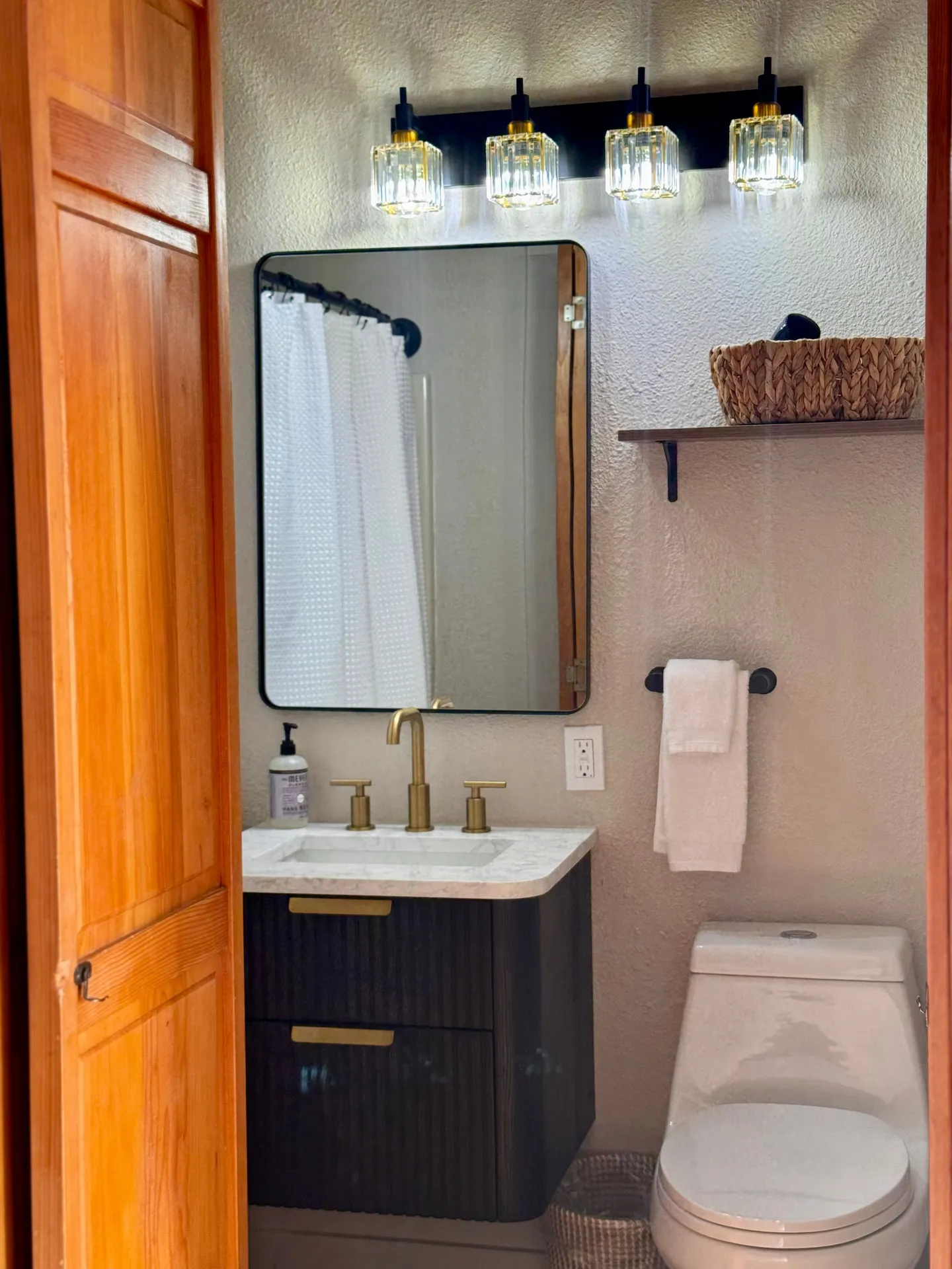Bathroom vanity with a dark fluted cabinet, brass faucet, rectangular mirror, modern light fixture, and toilet.