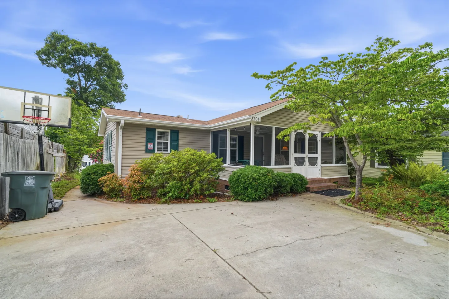 Front view of a single-story house featuring a concrete driveway, basketball hoop, and screened-in front porch.