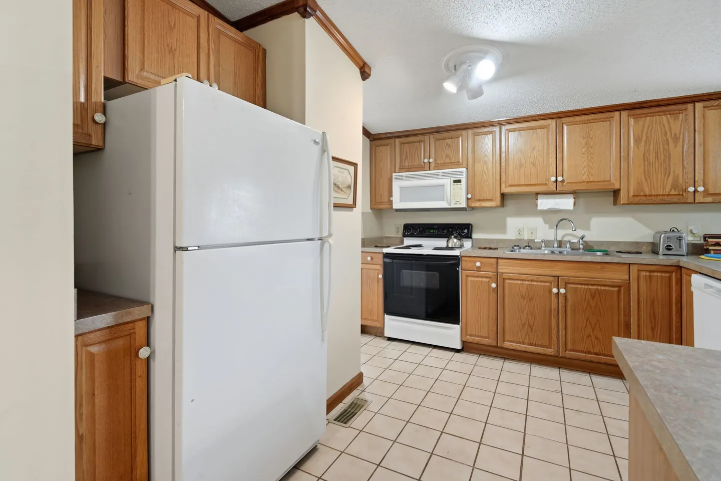Kitchen with oak cabinets, white refrigerator, black and white stove, and light-colored tile flooring.