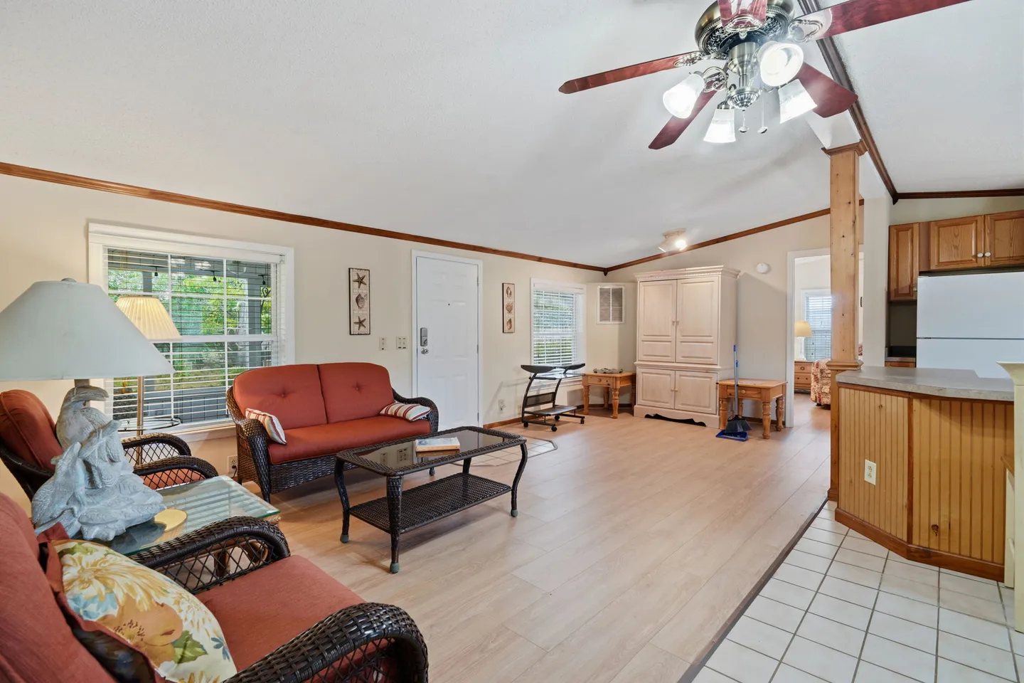 Living room with wicker seating with red cushions, light-colored flooring, vaulted ceiling with fan, and open view to the kitchen.