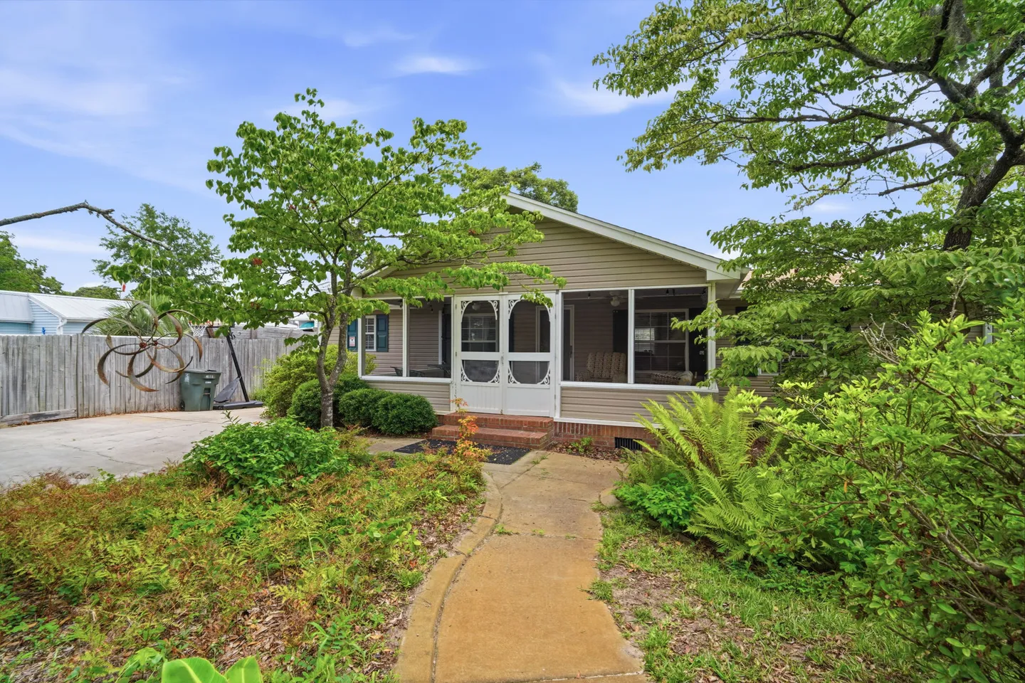 Exterior of a single-story home with a screened front porch, concrete walkway, and surrounding greenery.