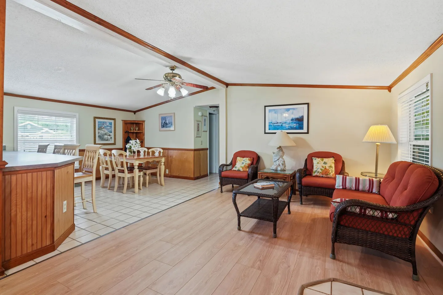 Open living area with wicker seating, adjacent to a dining space and kitchen counter with stools.
