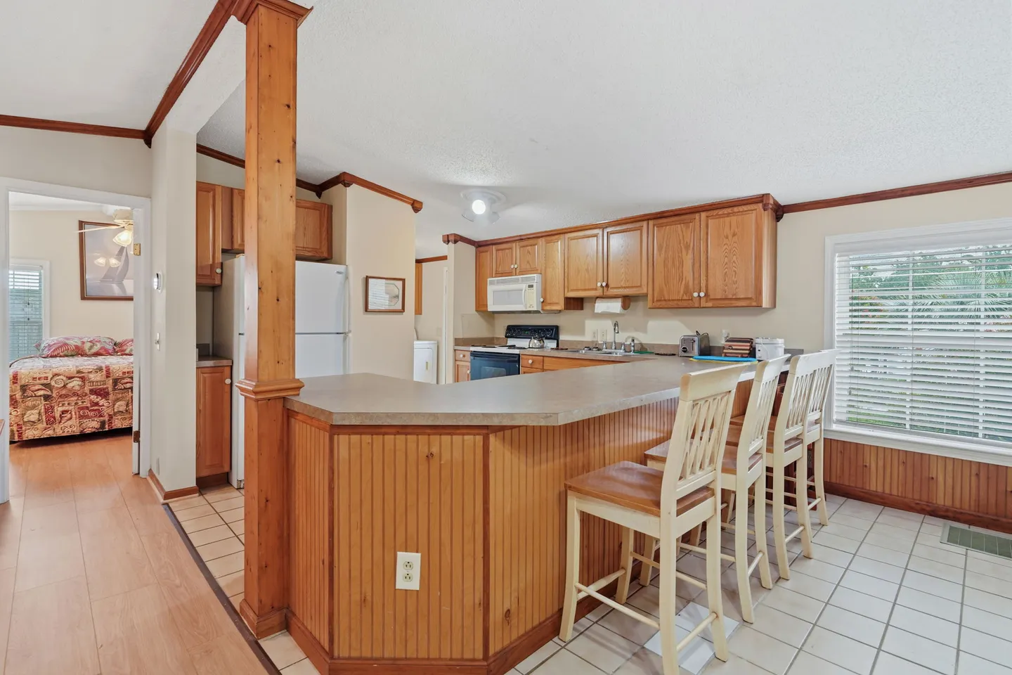 Kitchen with wood cabinetry, a breakfast bar with high chairs, and a view into an adjacent bedroom.