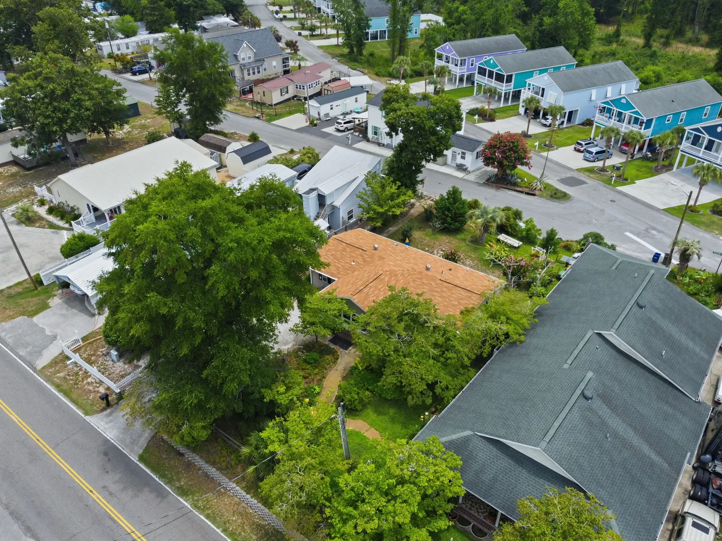 Aerial view of a single-story house with a brown shingle roof surrounded by green trees in a coastal neighborhood.