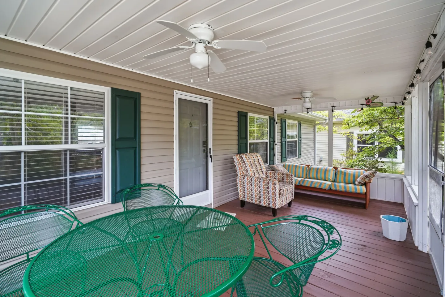 Screened porch with outdoor seating, green metal patio table and chairs, ceiling fans, and an exterior house door.