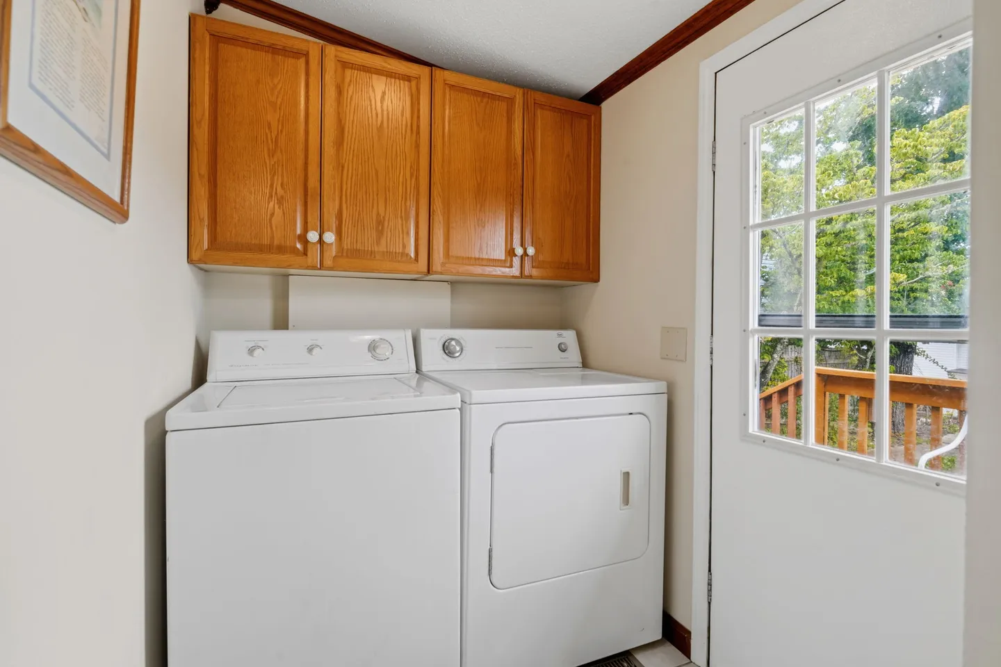 A laundry area with a white washer and dryer beneath wooden wall cabinets next to a glass-paneled exterior door.