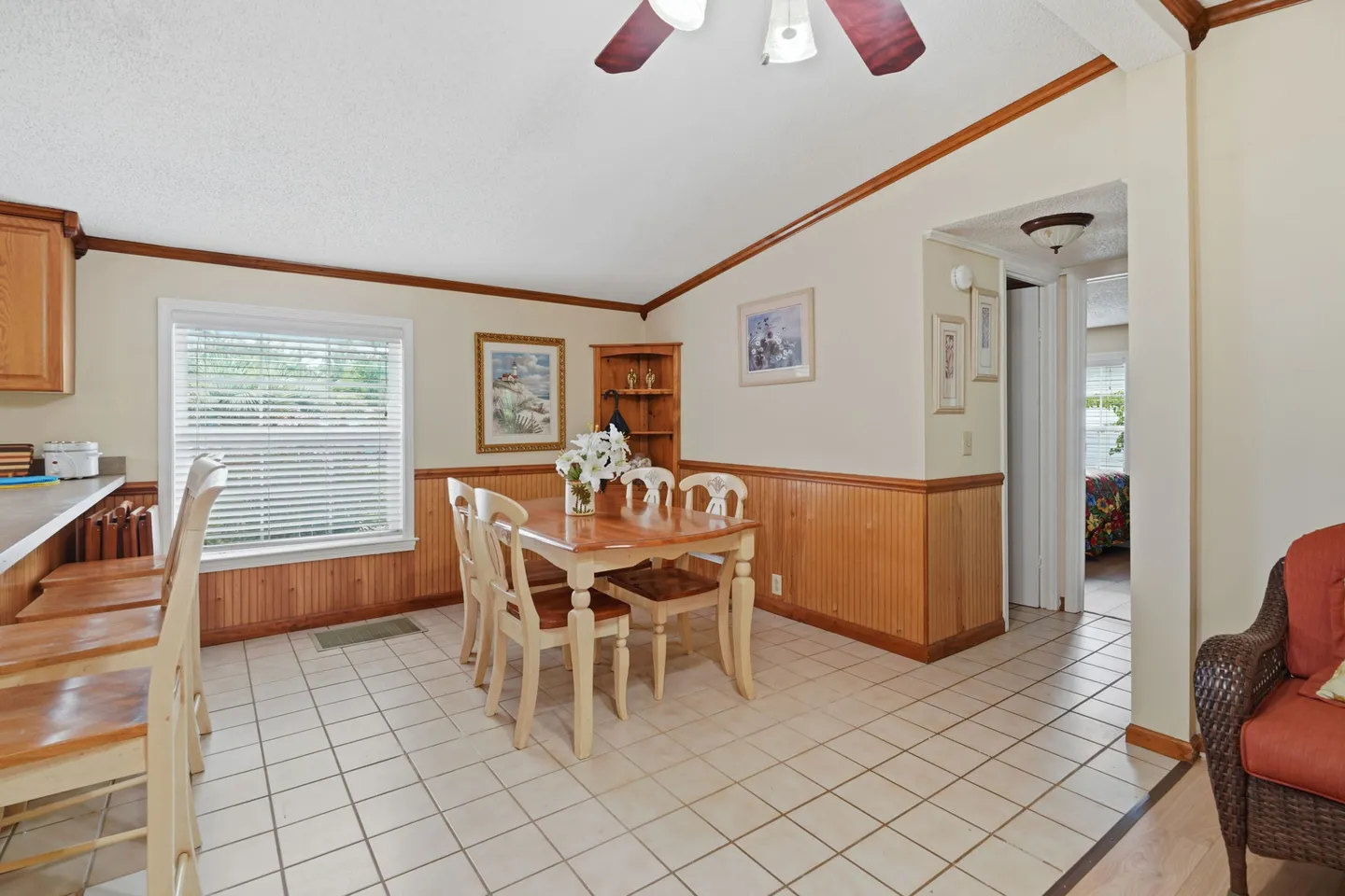 Dining area with tiled floors, wood wainscoting, and a wooden table with chairs under a vaulted ceiling.