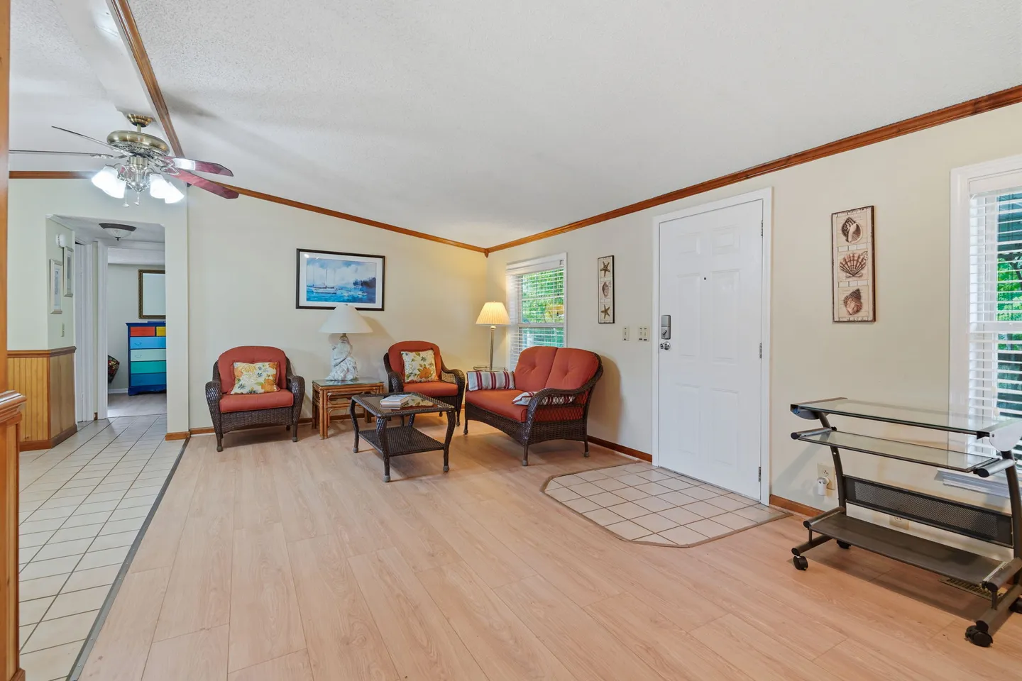 Living room with wicker seating, light wood-look flooring, ceiling fan, and front door entry.