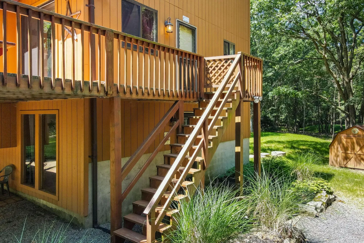 Exterior wooden staircase leading from the ground level to an elevated deck on a two-story home with yellow siding.