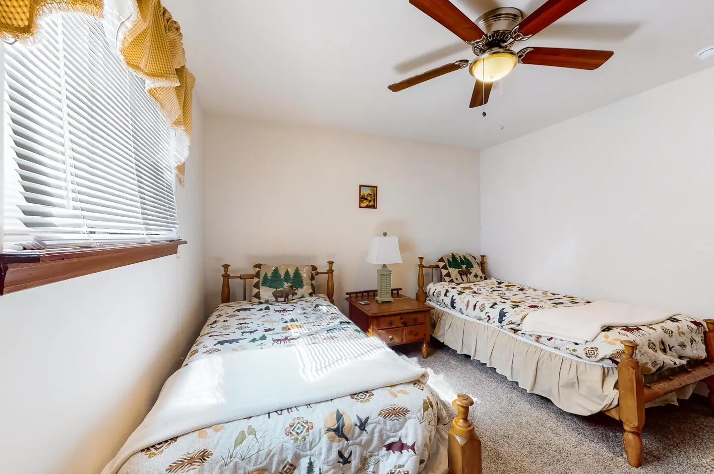 Bedroom with two twin wooden beds, patterned bedding, a nightstand with a lamp between them, and a ceiling fan.