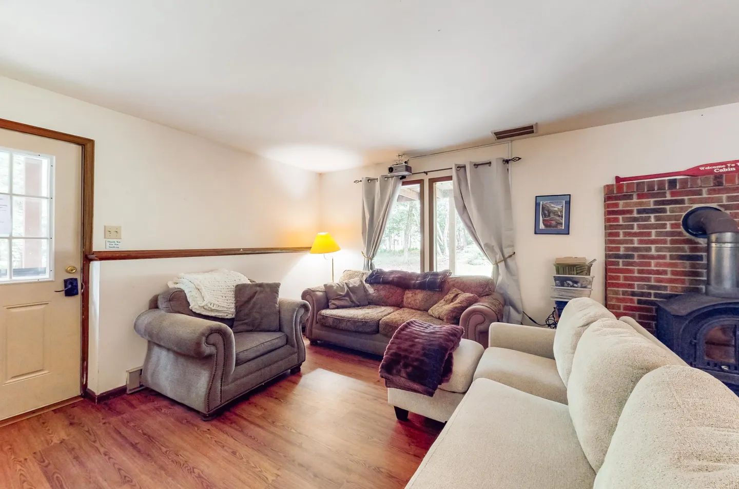 Living room with upholstered seating, an exterior door, a wood-burning stove with a brick backdrop, and wood-look flooring.