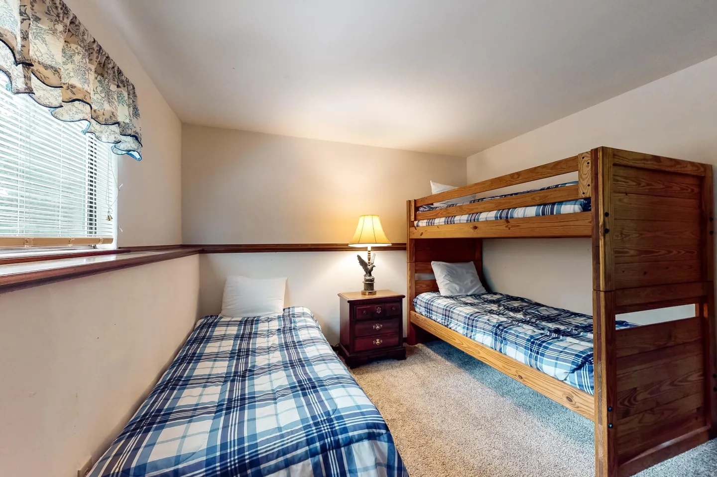 Bedroom with a single twin bed, wooden bunk beds, and a nightstand with a lamp.