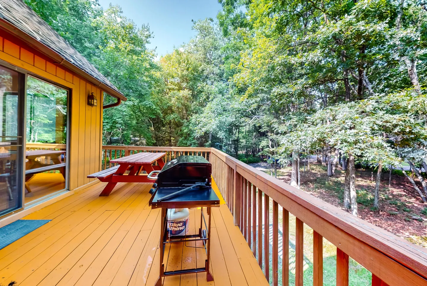 Elevated wooden deck with a picnic table and barbecue grill overlooking surrounding trees.
