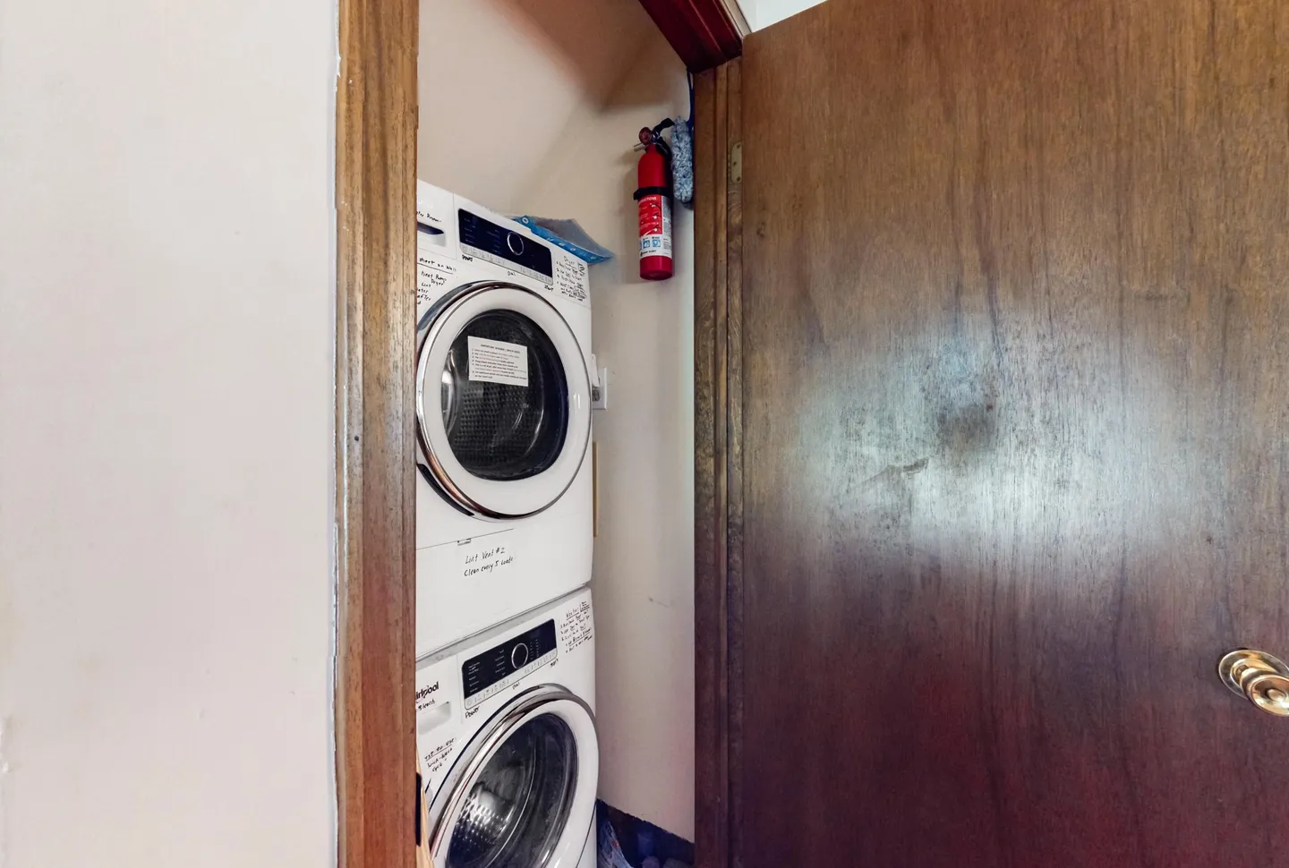 A stacked front-loading washer and dryer inside a small utility closet behind a wooden door.