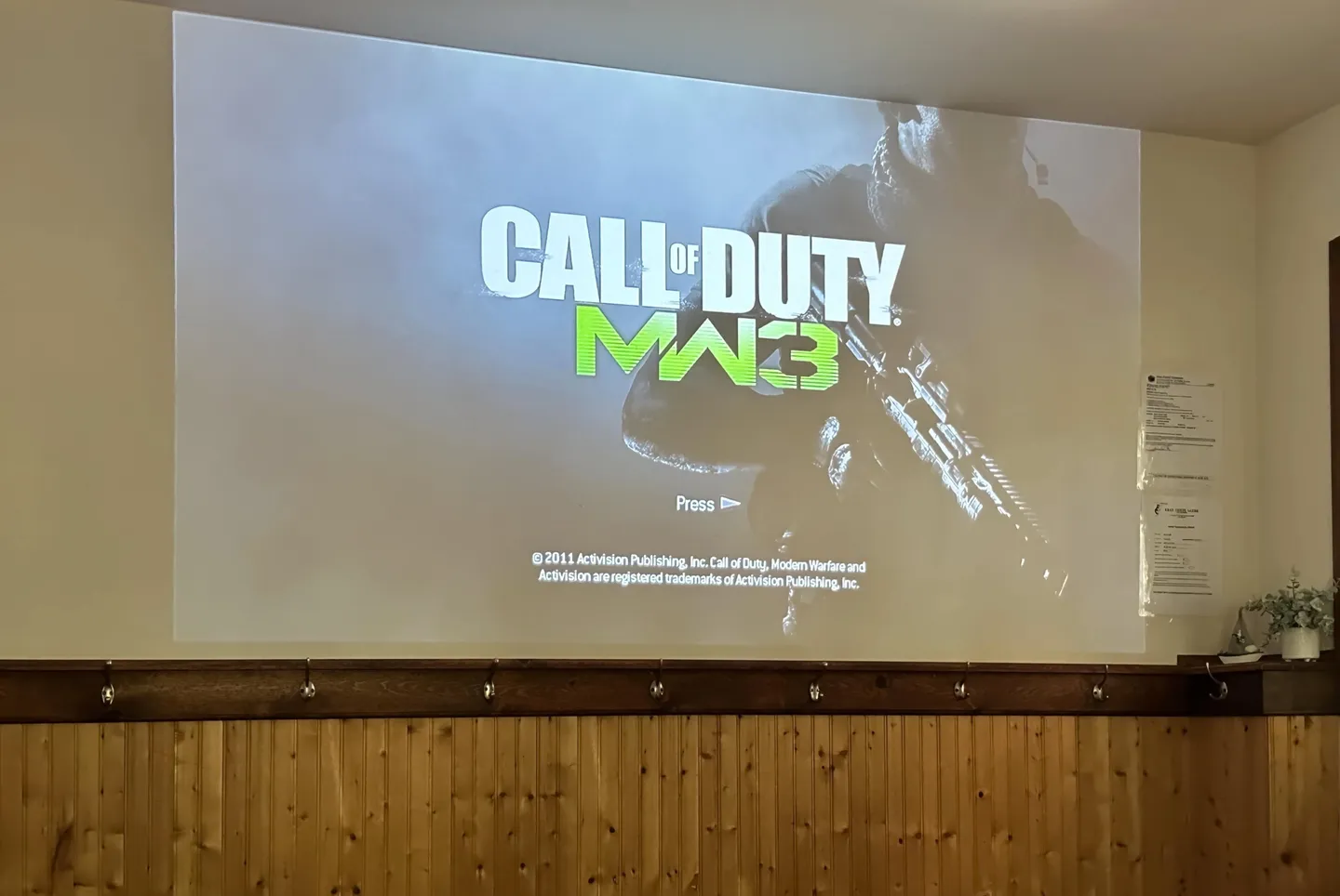A large projector screen displaying a video game title screen on a wall above wood wainscoting.