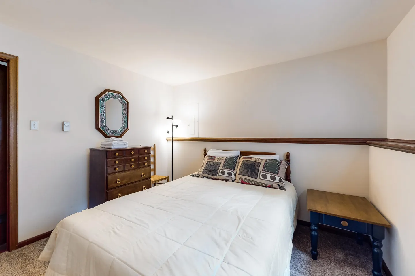 Bedroom with a bed, wooden dresser with a mirror, floor lamp, and a small side table.