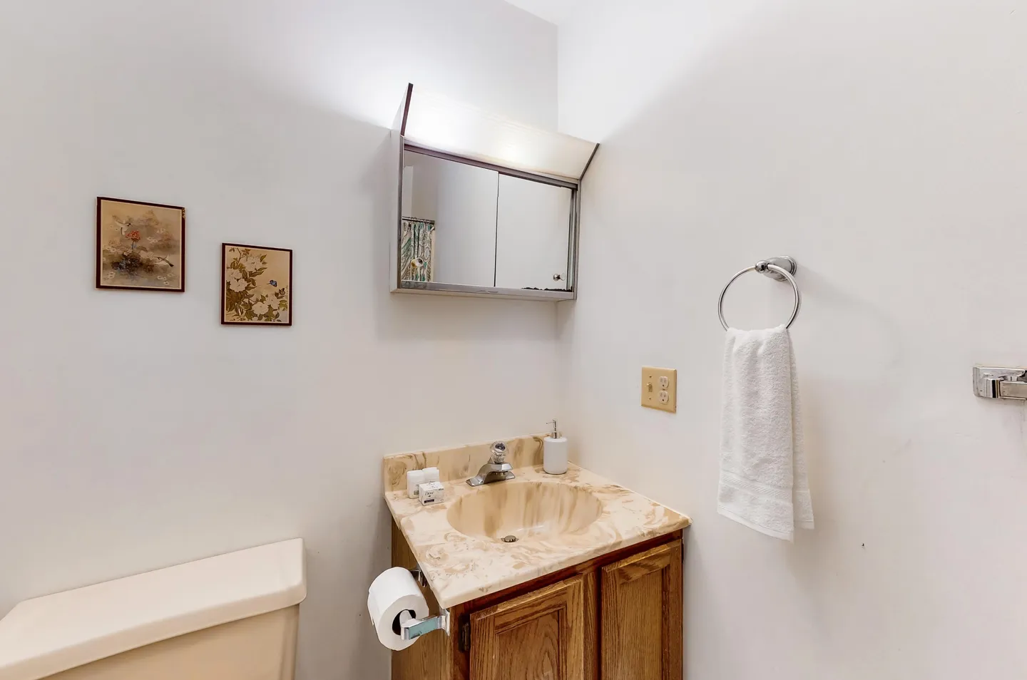 Bathroom vanity with a marbled sink, wooden cabinet, toilet tank, and mirrored medicine cabinet with overhead light.