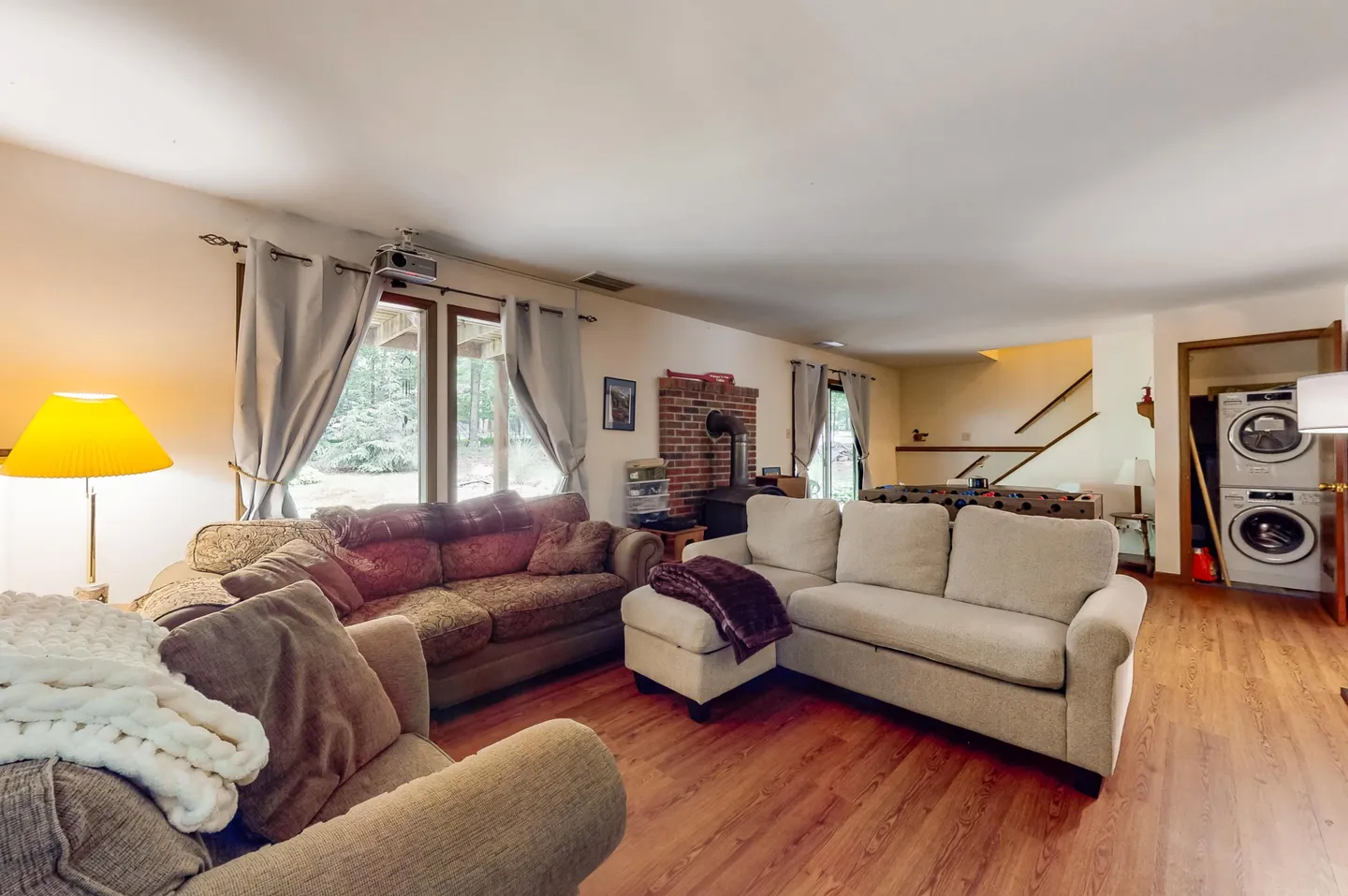 Living area with multiple sofas, wood-look flooring, a wood-burning stove against a brick backdrop, and a laundry closet in the background.