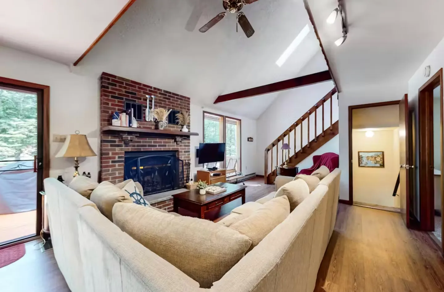 Living room with a large sectional sofa, brick fireplace, wooden staircase, and vaulted ceiling.