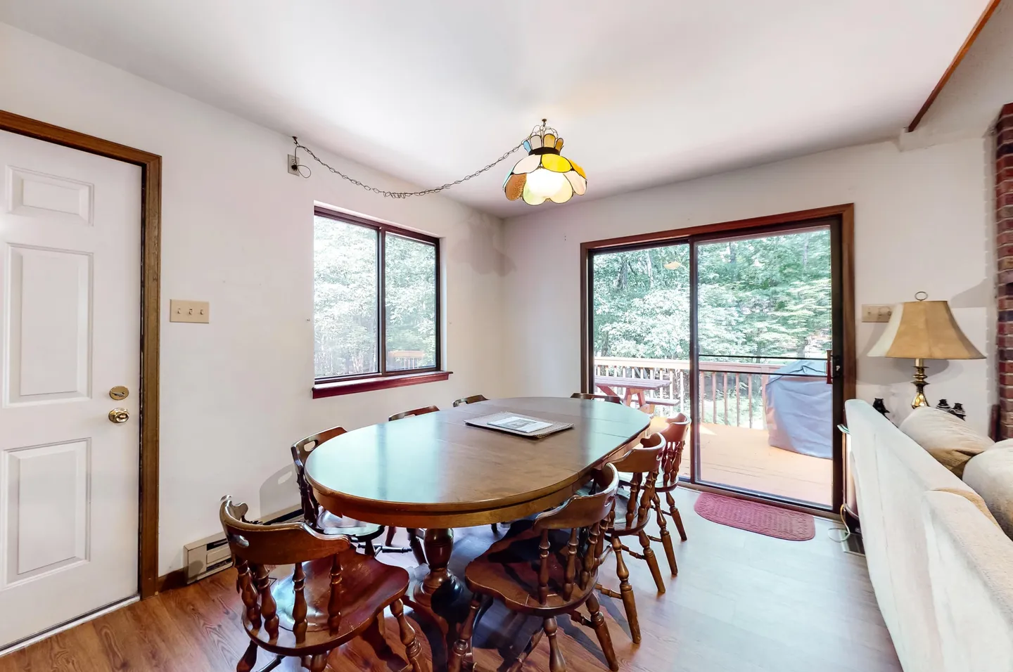 Dining area with an oval wooden table, matching wooden chairs, a hanging stained-glass style lamp, and sliding glass doors leading to a back deck.