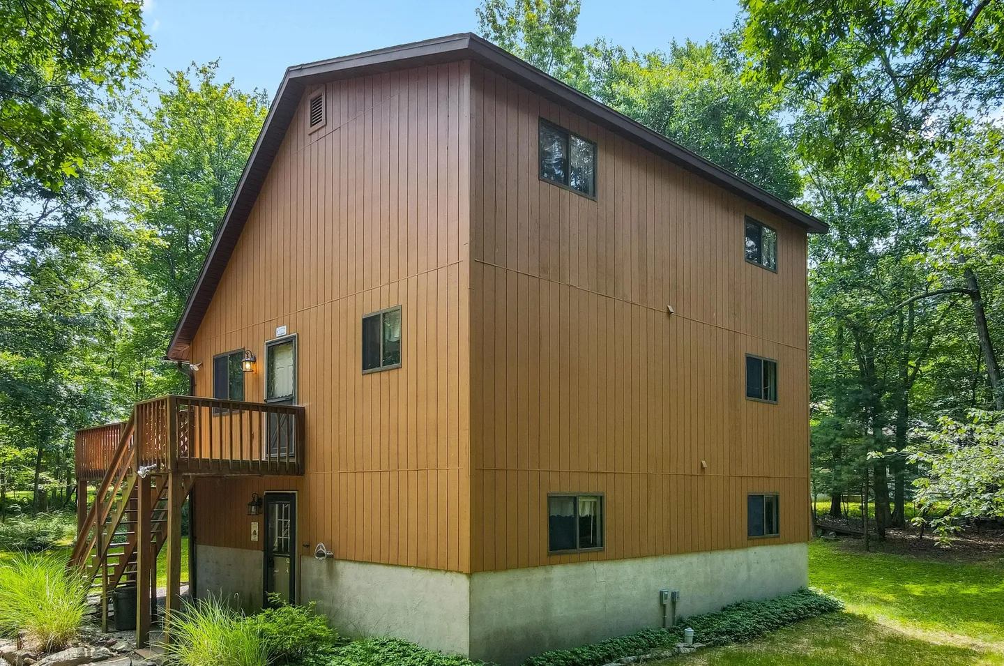 Exterior view of a multi-story brown vertical-sided house surrounded by trees with an outdoor wooden staircase and deck.