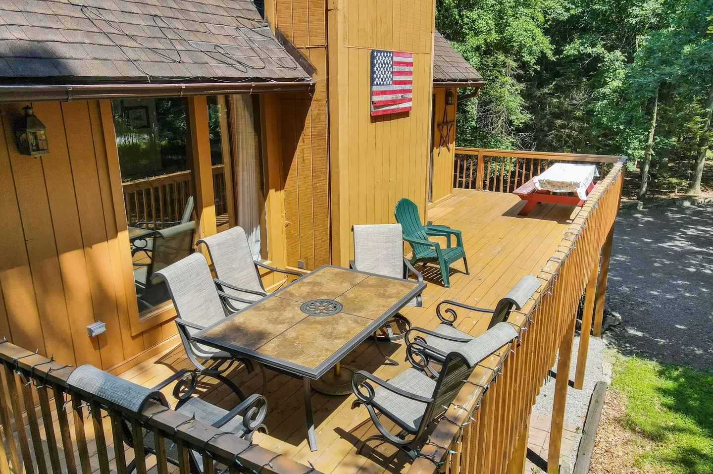 Elevated wooden deck with an outdoor dining table, chairs, a green armchair, and a picnic table.
