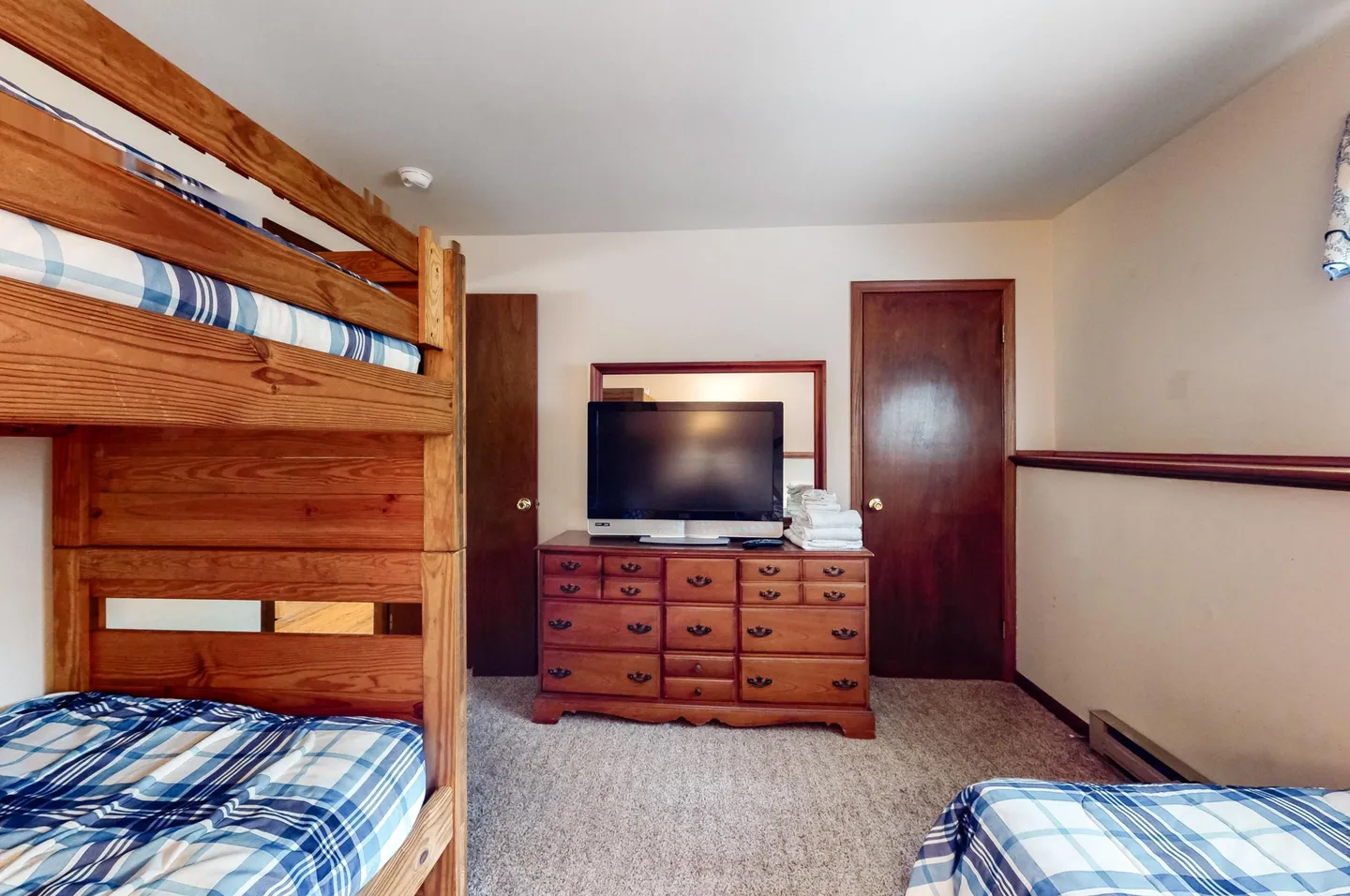 Bedroom with wooden bunk beds, carpeted flooring, a television atop a wooden dresser, and another bed in the foreground.