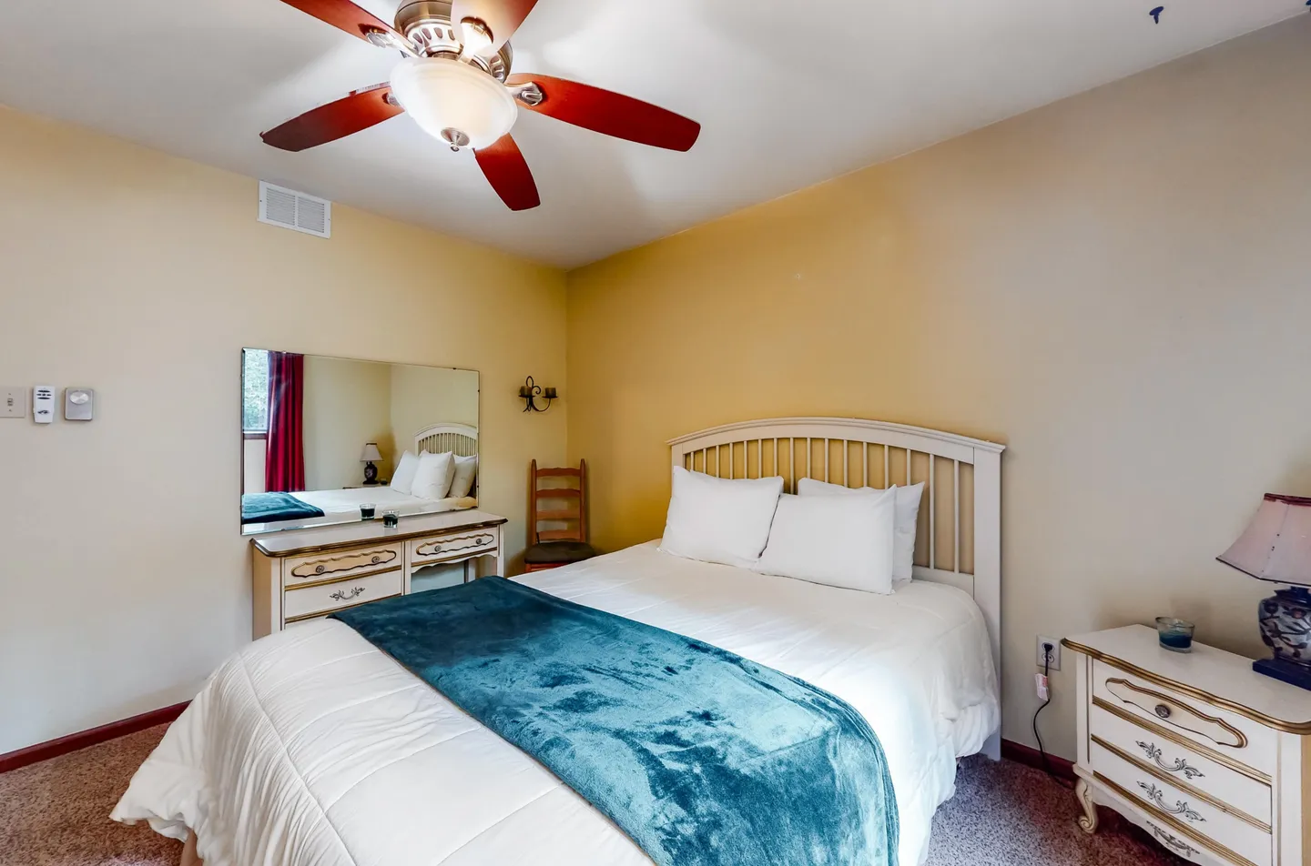 Bedroom with a white spindle bed, a blue throw blanket, matching light-colored nightstand and vanity, and a ceiling fan.