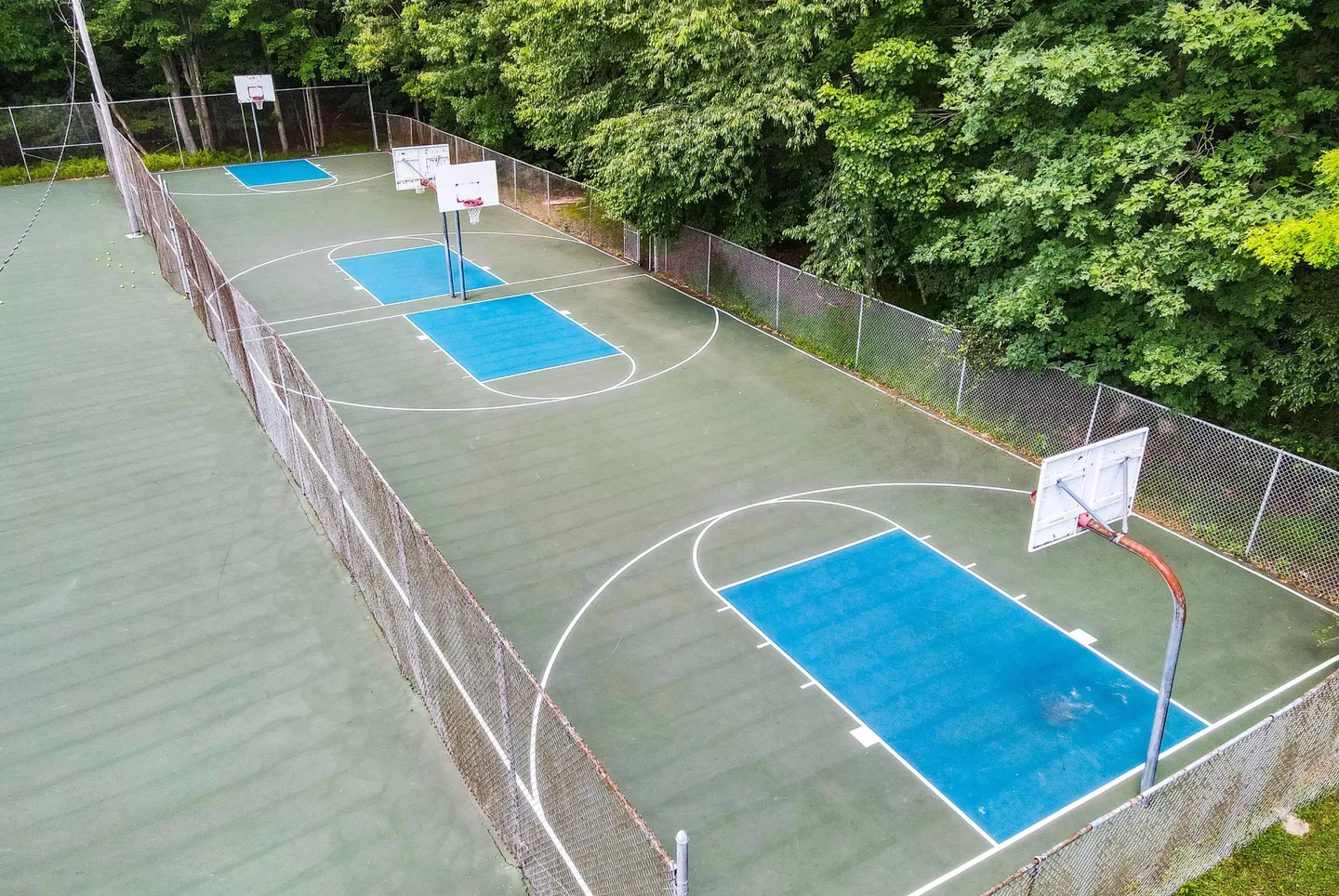 High-angle view of an outdoor fenced basketball court surrounded by dense green trees.