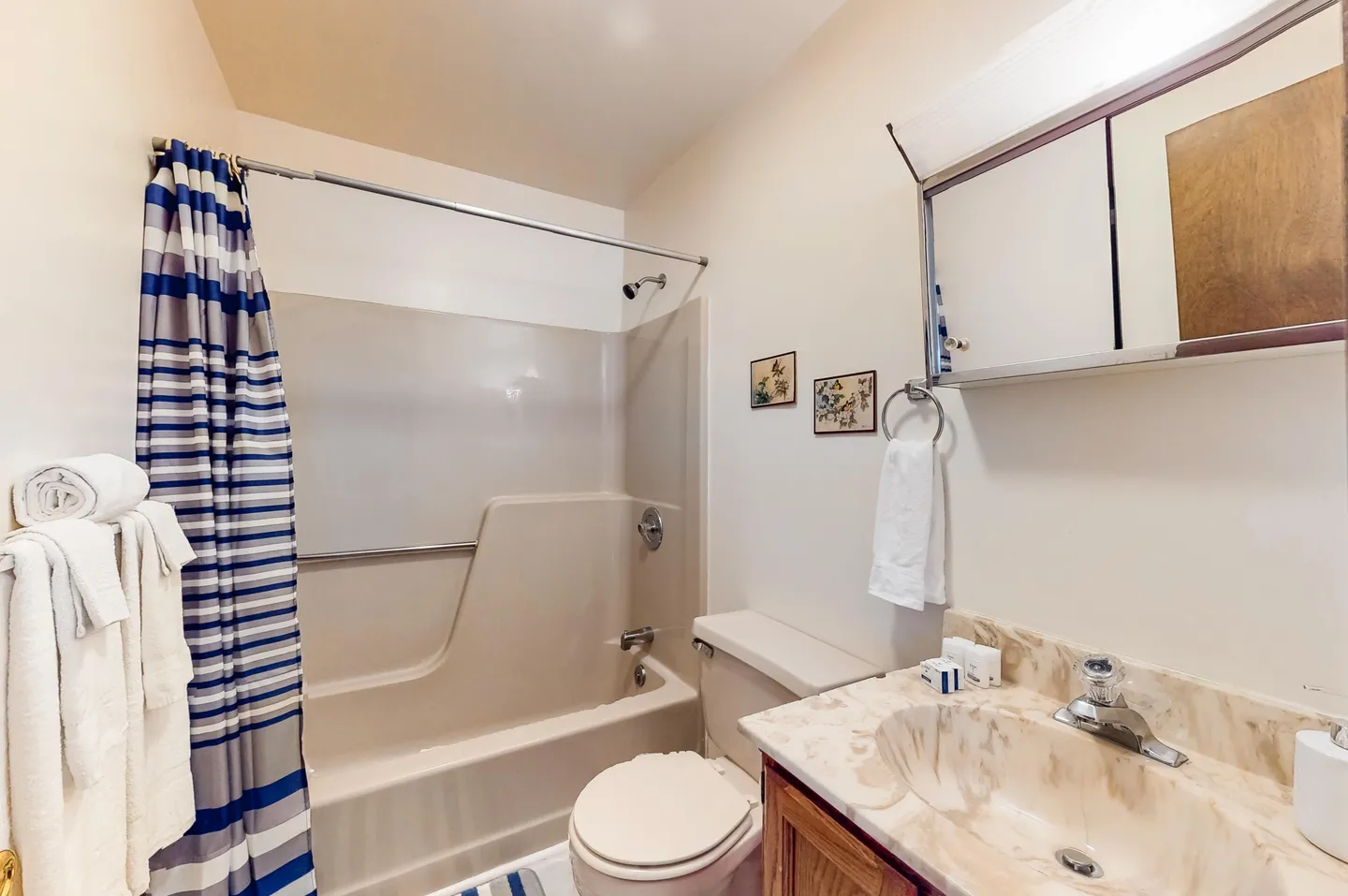 Bathroom with a bathtub and shower combination, striped shower curtain, toilet, and marble-look vanity sink.