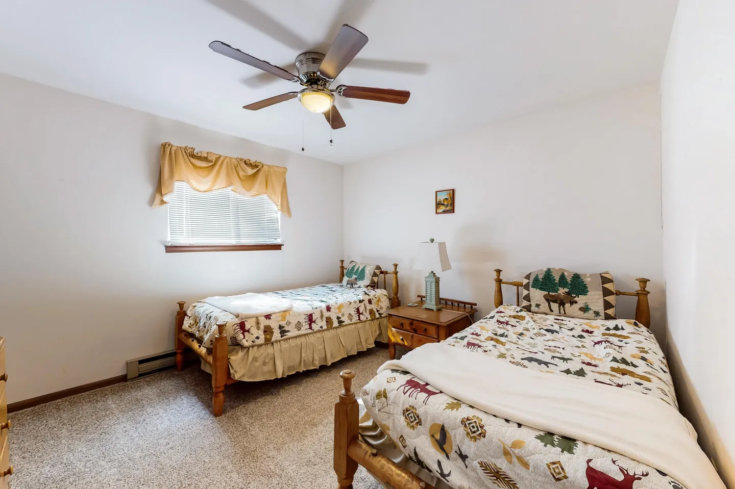 Bedroom with two twin beds featuring rustic woodland bedding, a nightstand, carpeted floor, and a ceiling fan.