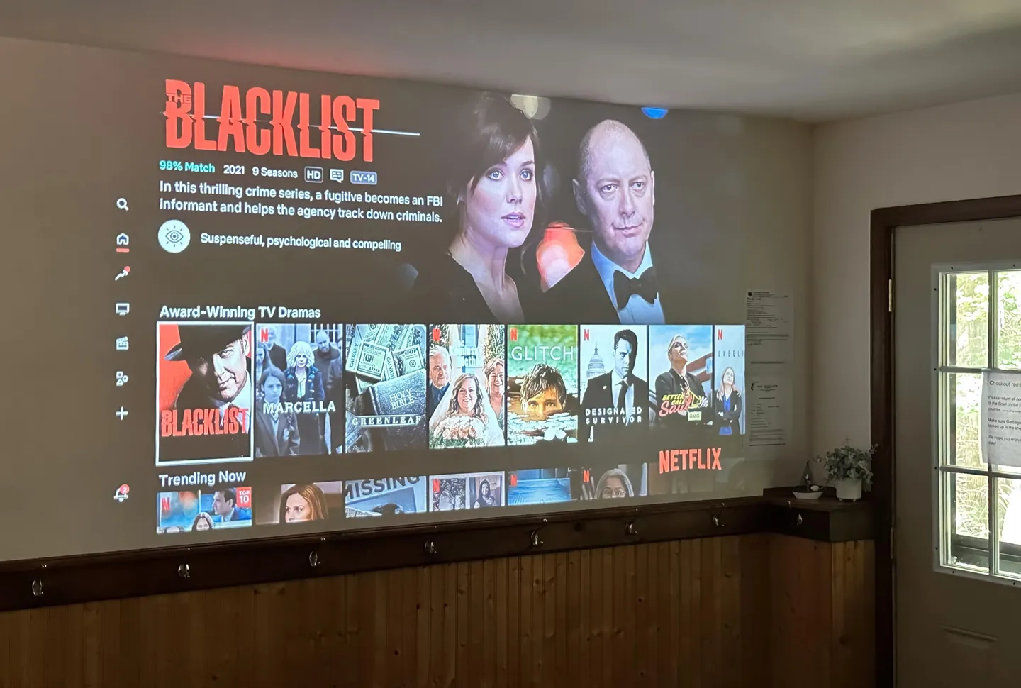 A movie streaming interface projected directly onto a white wall above wood paneling.